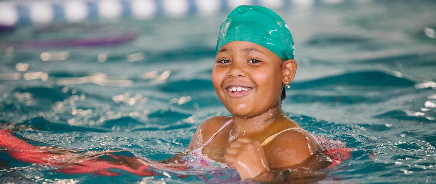 Young girl smiles while swimming in YMCA indoor pool in Castle Hill, Bronx