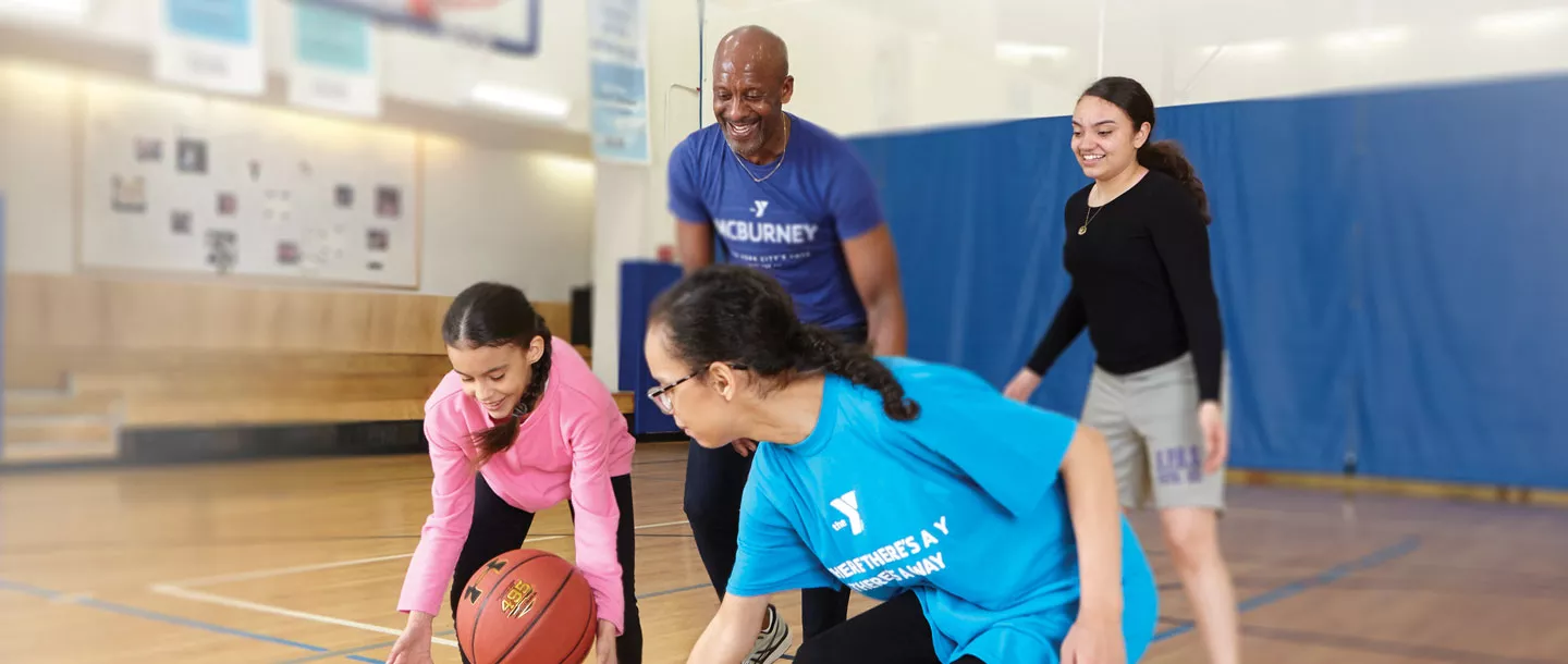 Three daughters playing basketball with their dad at McBurney YMCA indoor basketball court