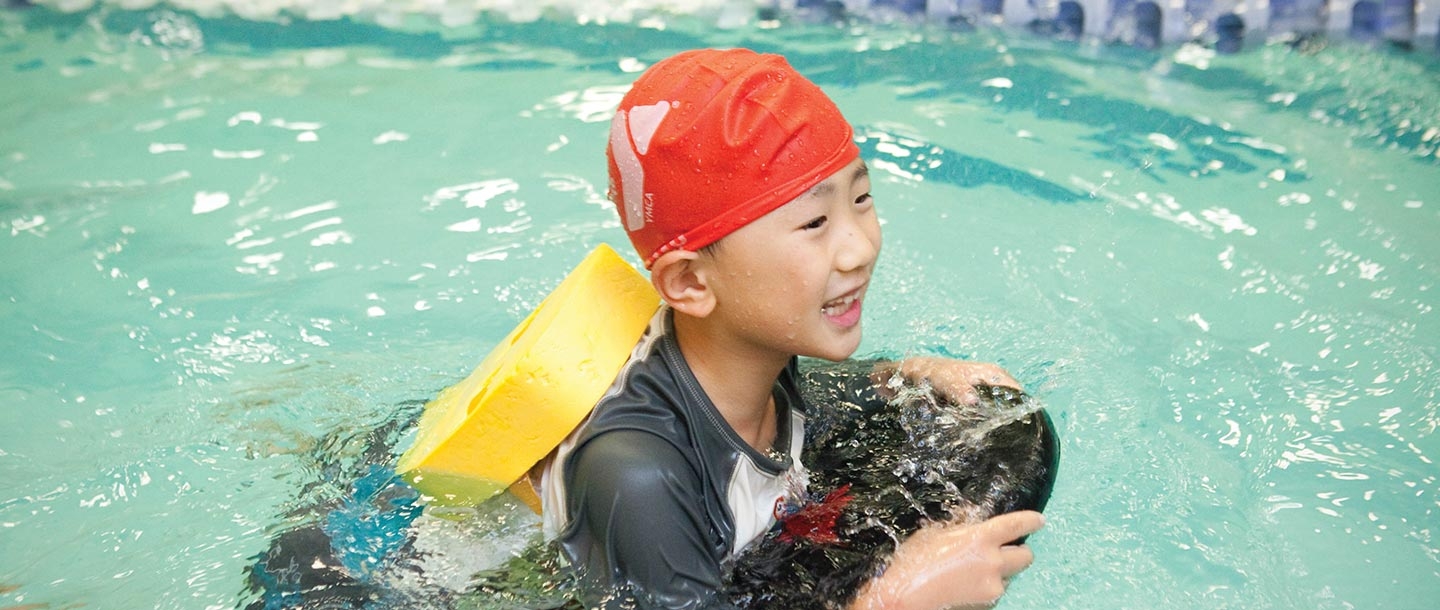 Boy with backpack and kickboard learns to swim at Vanderbilt YMCA summer camp