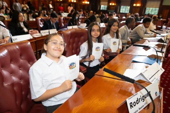Teens hold up programs in the City Hall chambers for TTC event.