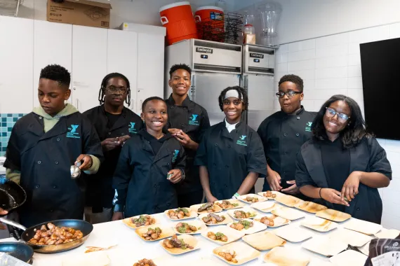Teens prepare meal around island in the NEBX Teaching Kitchen. 