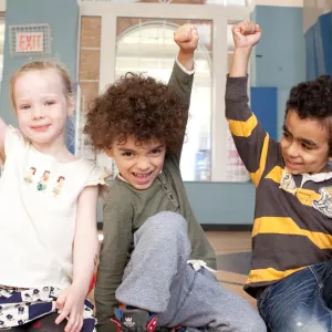 A diverse group of kids smile and raise their fists.