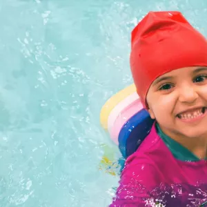 A preschool-aged child smiles in the pool during YMCA swim lessons.