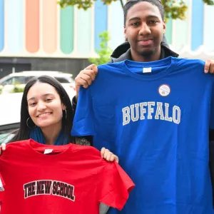 Four teens, supported by NYC's YMCA, hold up shirts with the name of colleges.