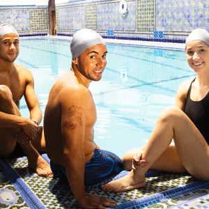Three swimmers sit poolside at the YMCA.