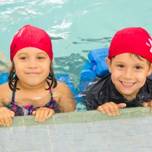 Group of preschool campers learning how to swim at indoor YMCA pool during summer camp