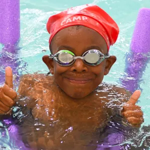 Campers having the best summer ever at the YMCA swimming in pool with noodle