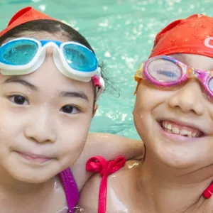 Two girls swimming during YMCA summer camp in indoor pool in Flushing, Queens