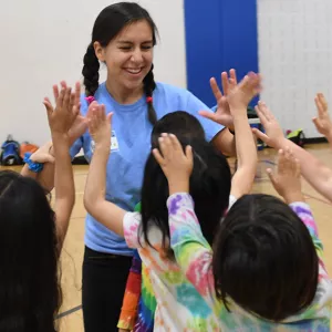 Camp counselor high fiving group of children at LIC YMCA gym
