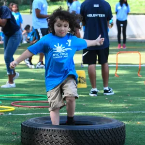 Child running through obstacle course tire outside in North Brooklyn YMCA summer camp
