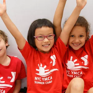 Three kids smile while wearing YMCA Day Camp shirts.