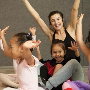 Three ballerina girls with YMCA instructor and arms up