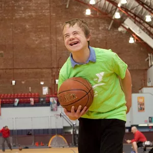 Boy in green t-shirt smiling with basketball at indoor YMCA gymnasium