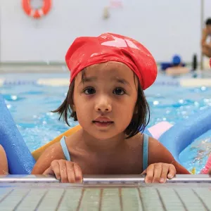 Three girls hold the side of LIC YMCA's indoor pool during camp swim