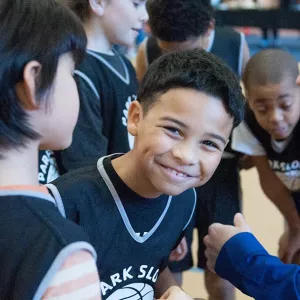 Boy smiling in group of basketball players at Park Slope Armory YMCA basketball league on indoor court