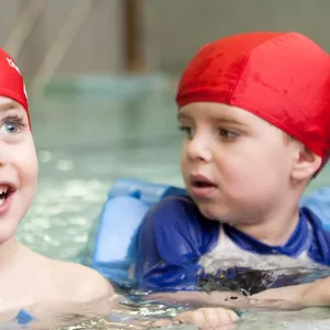 Preschool boys holding onto side of indoor YMCA pool during swim class