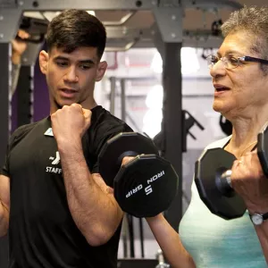Personal trainer demonstrates how to lift weights with client at YMCA