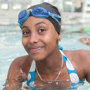 Teen girl gives thumbs up while swimming at Rockaway YMCA indoor pool in Queens