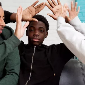 Three teen boys high five each other at YMCA teen center