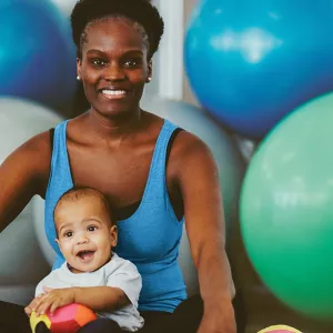 Mom sitting on yoga mat with baby and exercise balls