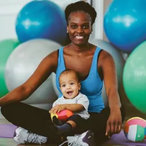 Mom sitting on yoga mat with baby and exercise balls