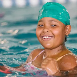 Young girl smiles while swimming in YMCA indoor pool in Castle Hill, Bronx