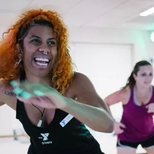 YMCA zumba instructor smiling while swinging her arms and leading class in fitness studio at Ridgewood YMCA