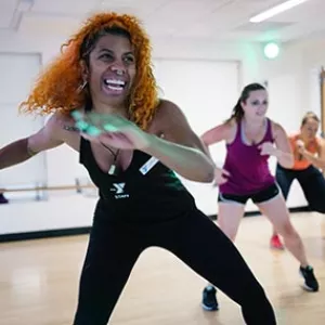 YMCA zumba instructor smiling while swinging her arms and leading class in fitness studio at Ridgewood YMCA