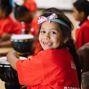Girl with headband smiling while playing drums at Castle Hill YMCA 