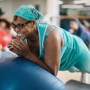 Woman with aqua bandana smiles while doing core exercises during Rockaway YMCA pilates mat class