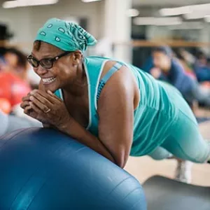 Woman with aqua bandana smiles while doing core exercises during Rockaway YMCA pilates mat class
