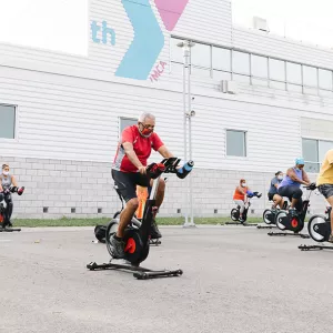 Many participants exercise on spin bikes outdoors in a YMCA outdoor fitness class.