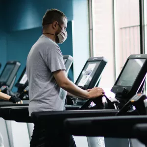 Two YMCA members work out on treadmills, socially distanced, while wearing masks.