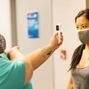 A YMCA member wearing a mask gets her temperature checked by a Y staff member.