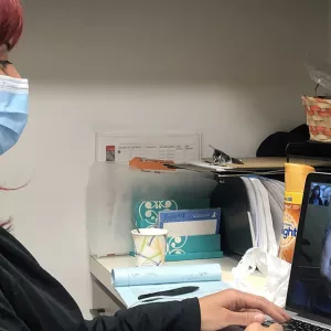 A person in a mask does a virtual call with a senior.