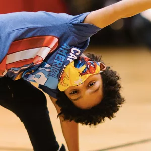 A boy wearing a mask does a yoga pose at the YMCA.