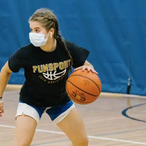 A girl in a mask plays basketball at the YMCA.