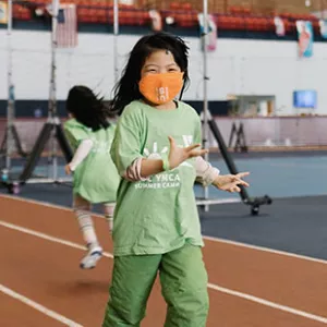 A girl wearing a mask smiles during camp at the YMCA.