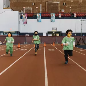 A group of kids in masks race on an indoor track during camp at the YMCA.
