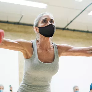 A woman wearing a mask lifting weights in a group exercise class