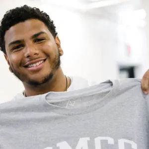 Y teen boy smiling and holding up a t-shirt of his future college