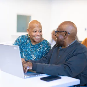 An older Black couple smiles at each other during a computer literacy class.
