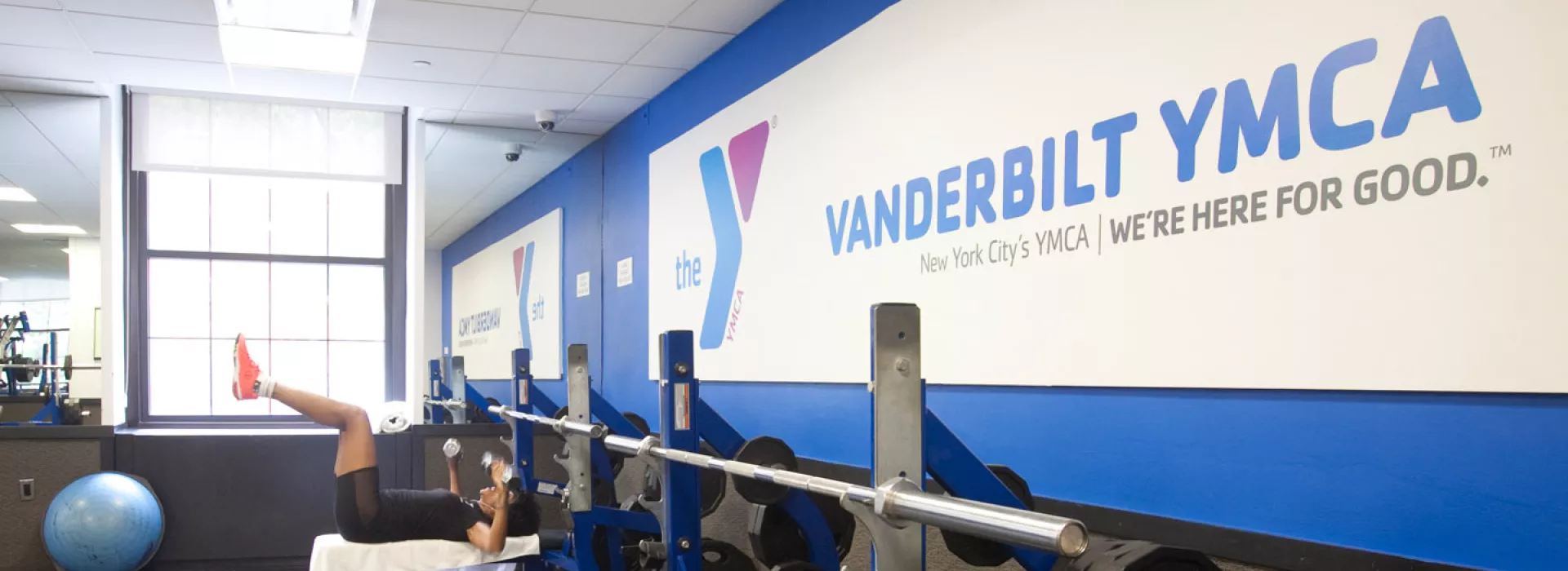 A woman lifts weights in the sunlit Vanderbilt YMCA weight room.