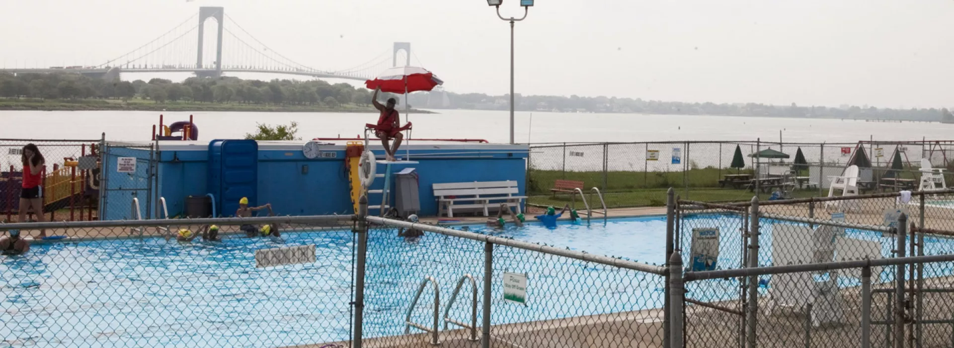 An outdoor pool at the Bronx YMCA, with bridge in background.