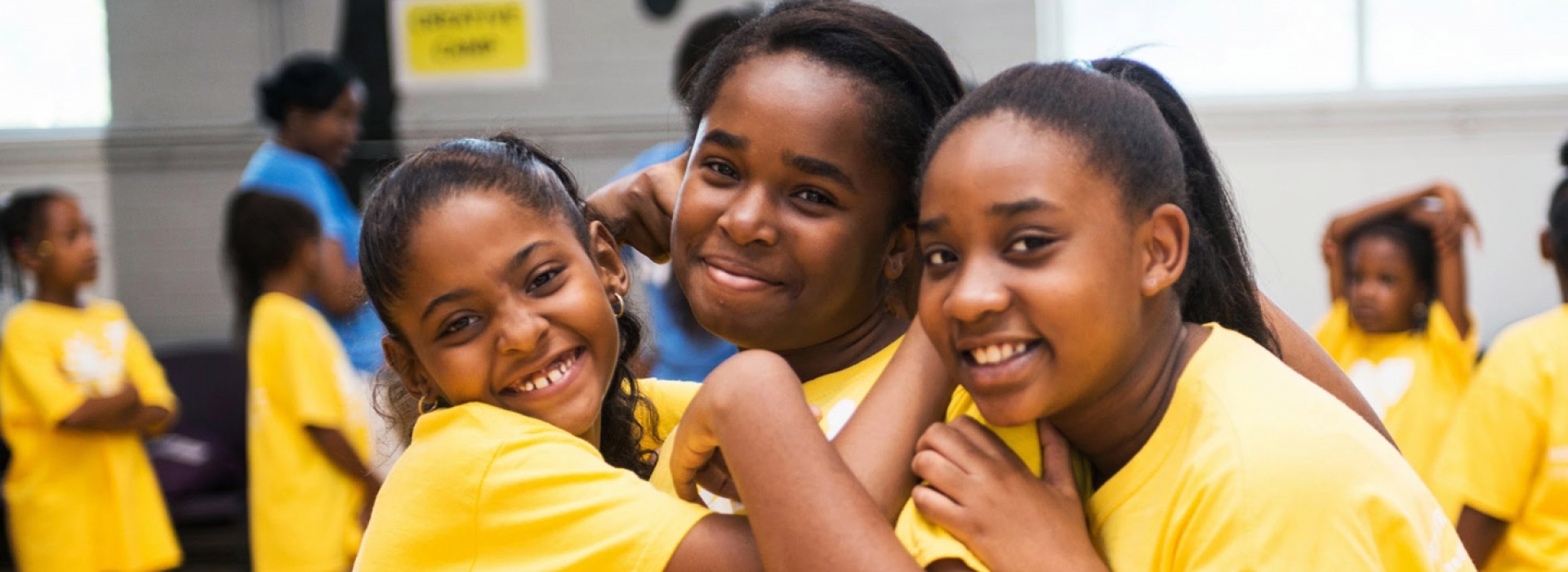 Three girls in YMCA camp t-shirts hug each other.