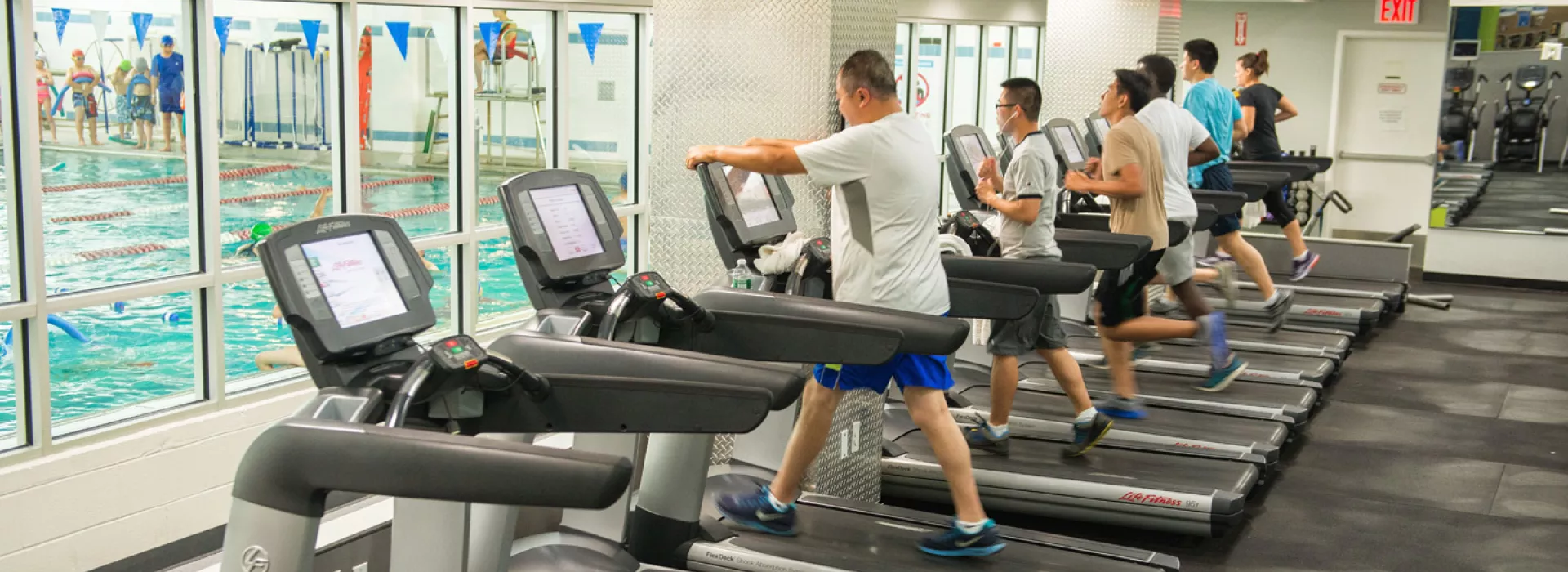 Chinatown YMCA members work out on treadmills, overlooking an indoor pool.