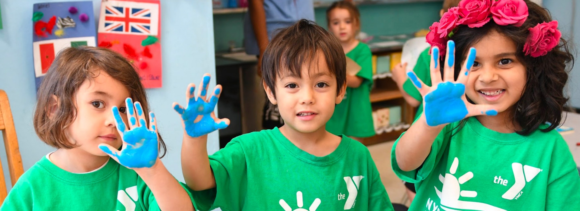 Three kids hold up paint-stained hands at the McBurney YMCA summer day camp.