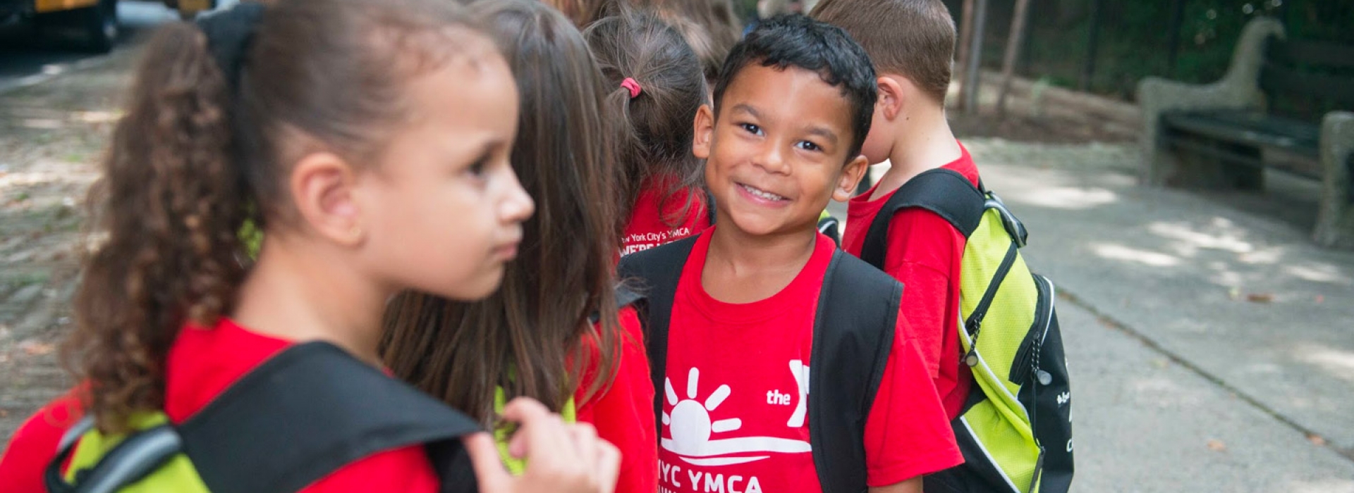A boy at the Ridgewood YMCA summer day camp smiles while standing outside with a group.