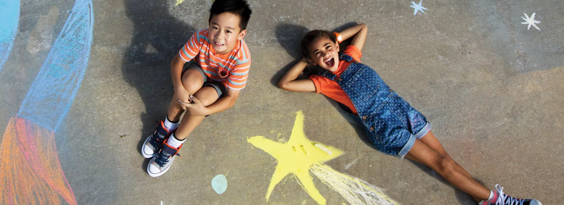 Two kids lying on the ground with chalk drawings.