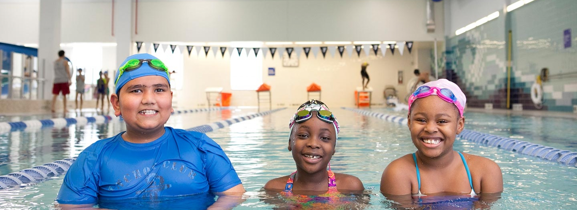 Three kids learning to swim in lap lane of indoor YMCA pool